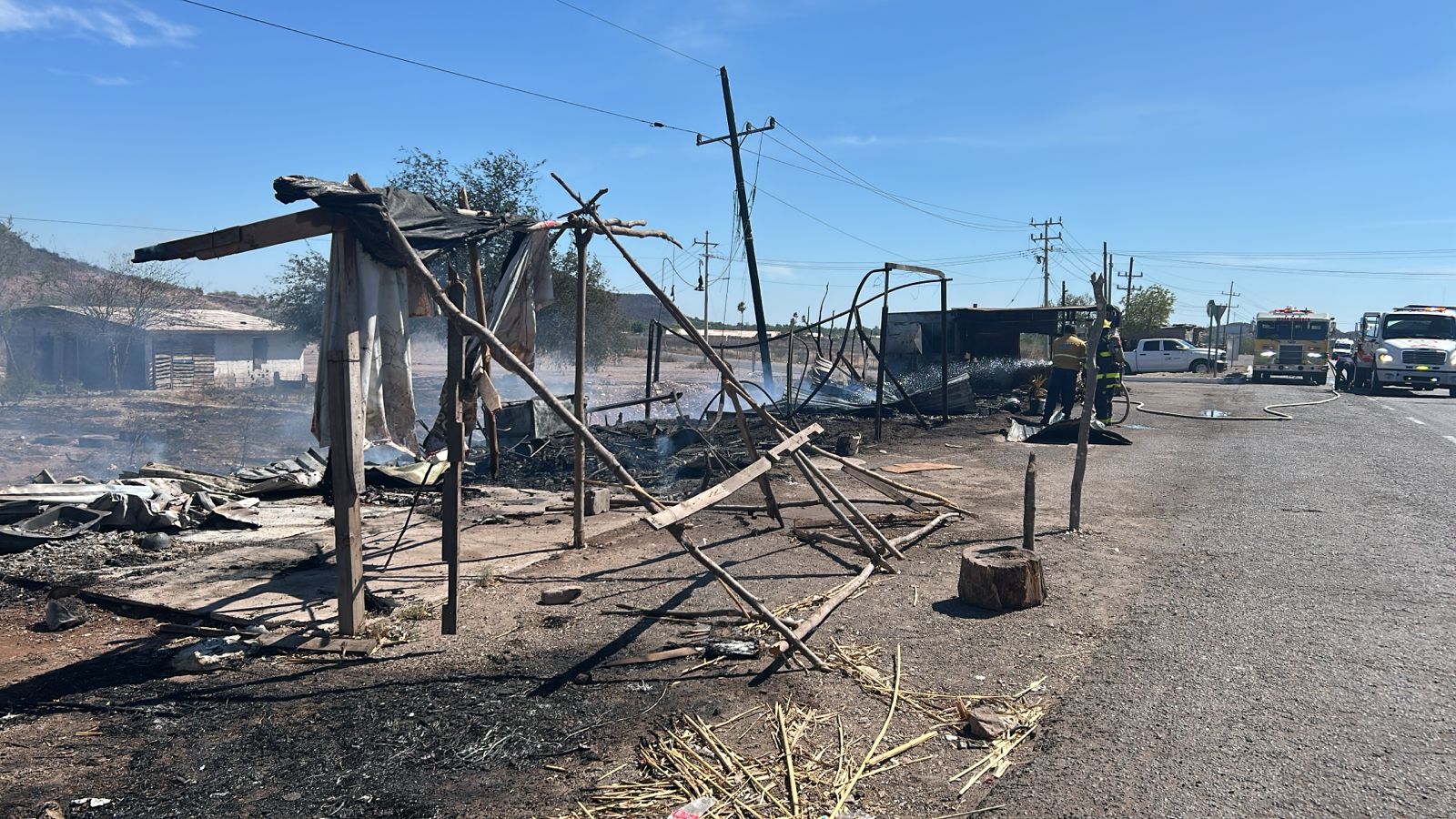 Local de madera completamente dañado por un incendio y bomberos asistiendo el incidente
