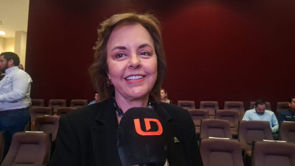 Mujer sonriendo viendo hacia el frente con un micrófono negro con las letras LD de color naranja