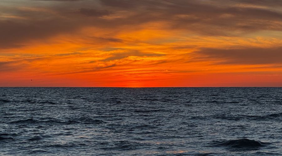 En el cielo se presenta un atardecer, colores cálidos y ciertas nubes, debajo el mar con presencia de oleaje