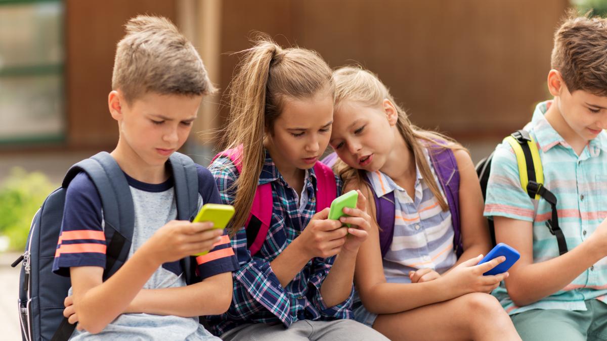 Niños sentados viendo sus celulares