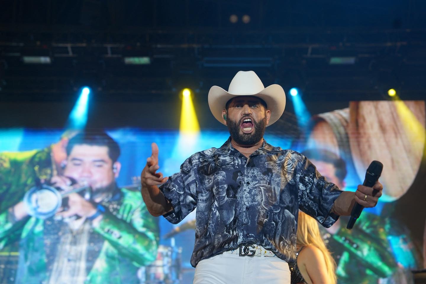 Pancho Barraza cantando en un escenario con pantalla y luces detrás