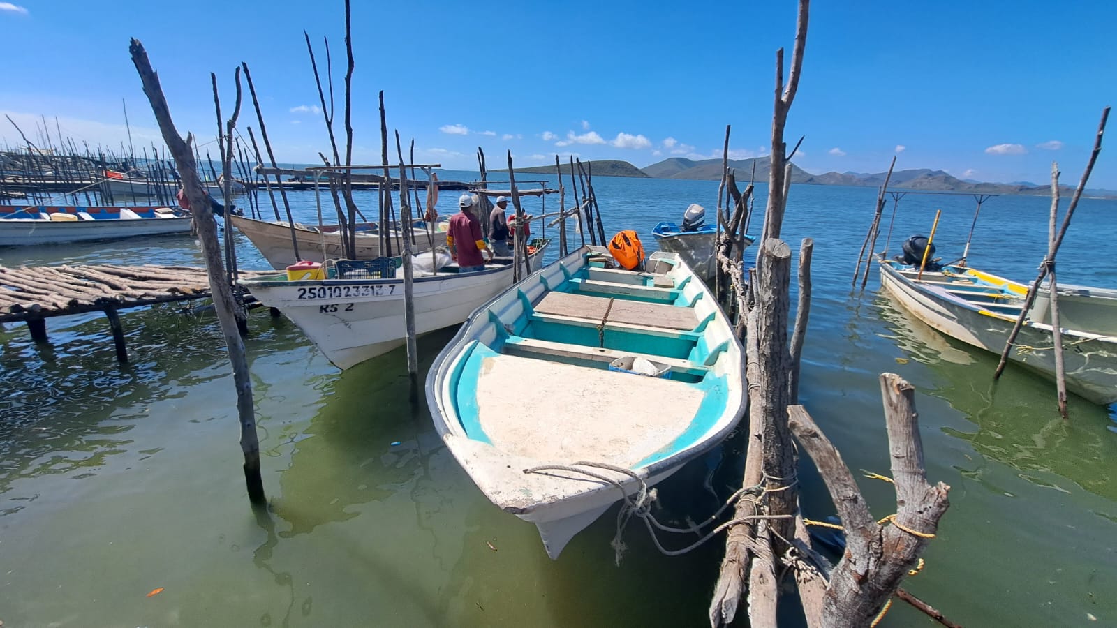 Lancha de pesca estacionada en orilla de puerto y pescadores arriba de ella