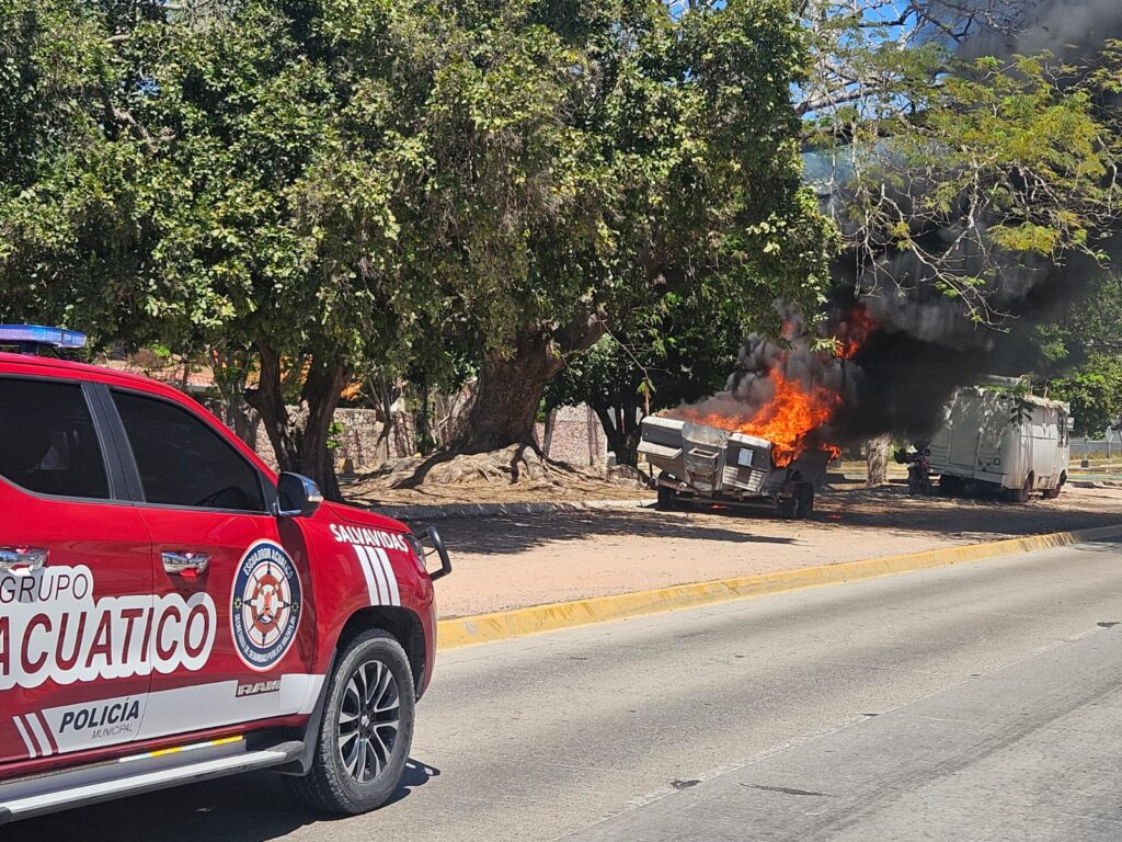 Camioneta de bomberos junto a embarcación con humo negro