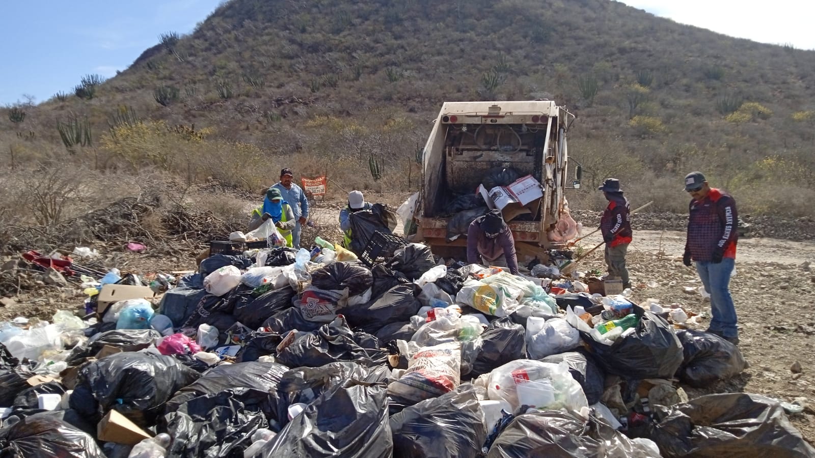 Montaña de bolsas de basura junto a camión recolector y personal del ayuntamiento