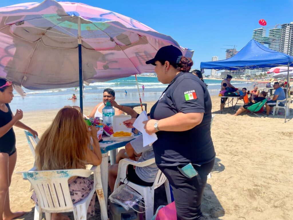 Una policía municipal entregando pulsera a cuatro turistas en una mesa con una sombrilla