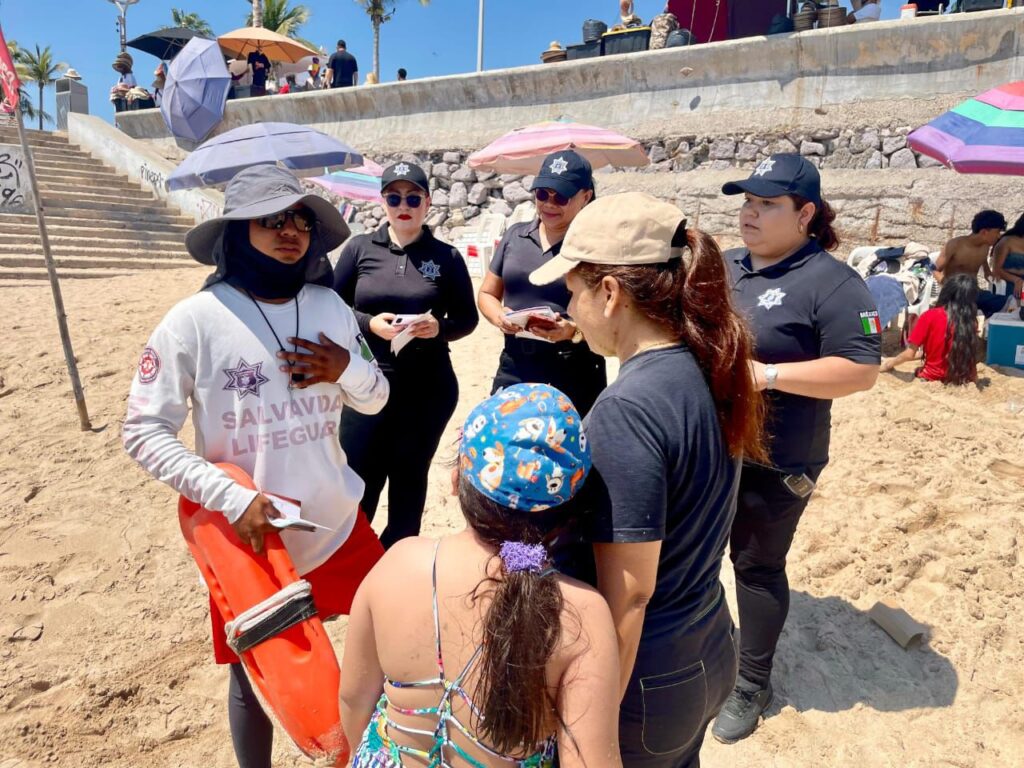 Elementos de seguridad junto a una persona con sobrero y turistas en la arena