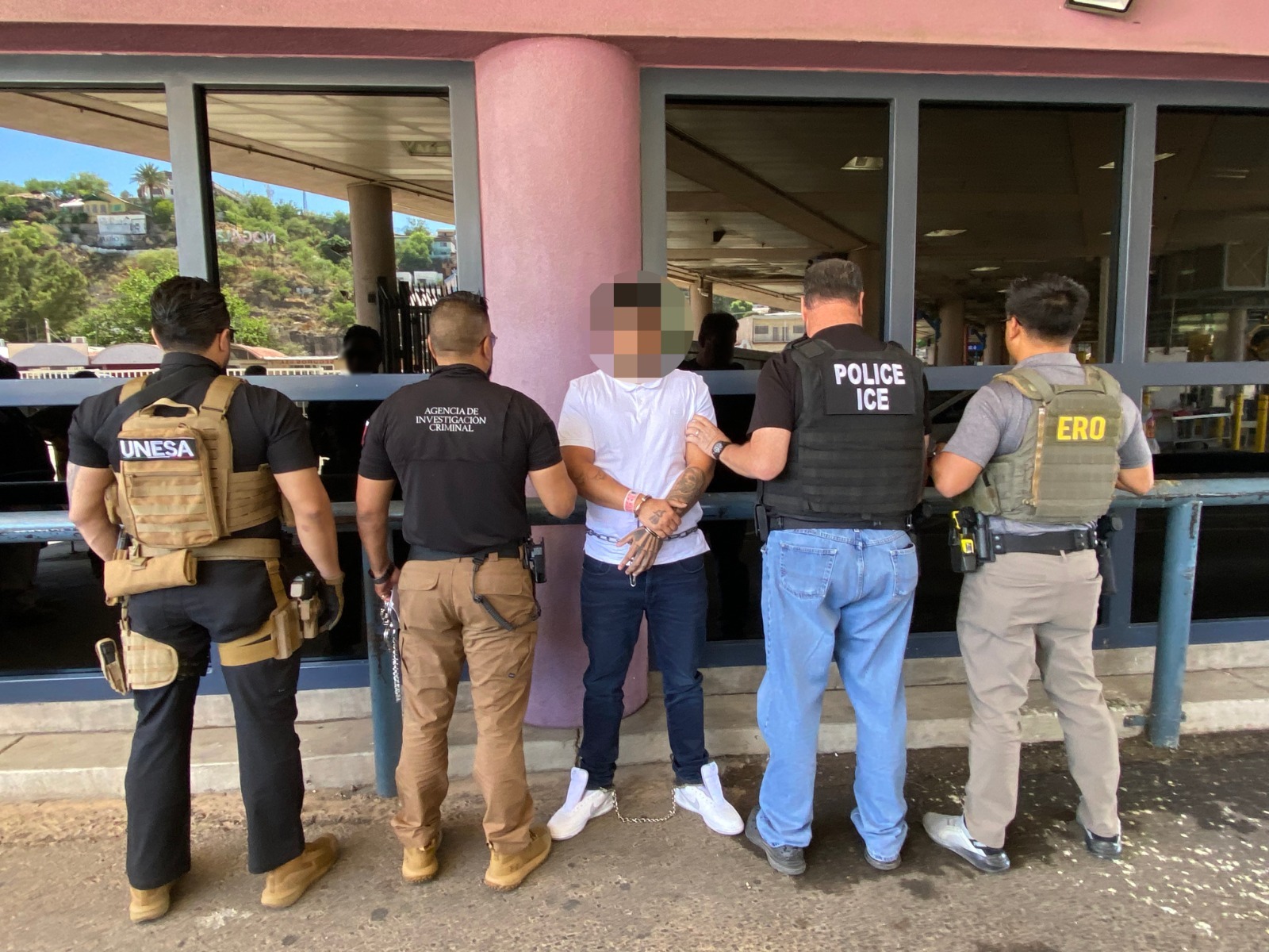 Elementos de seguridad de espaldas aprendiendo a un detenido con la cara blureada
