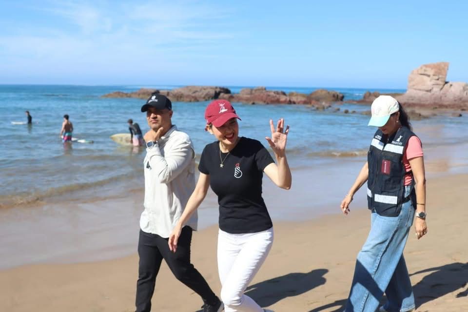 Estrella Palacios saludando con dos personas en la playa