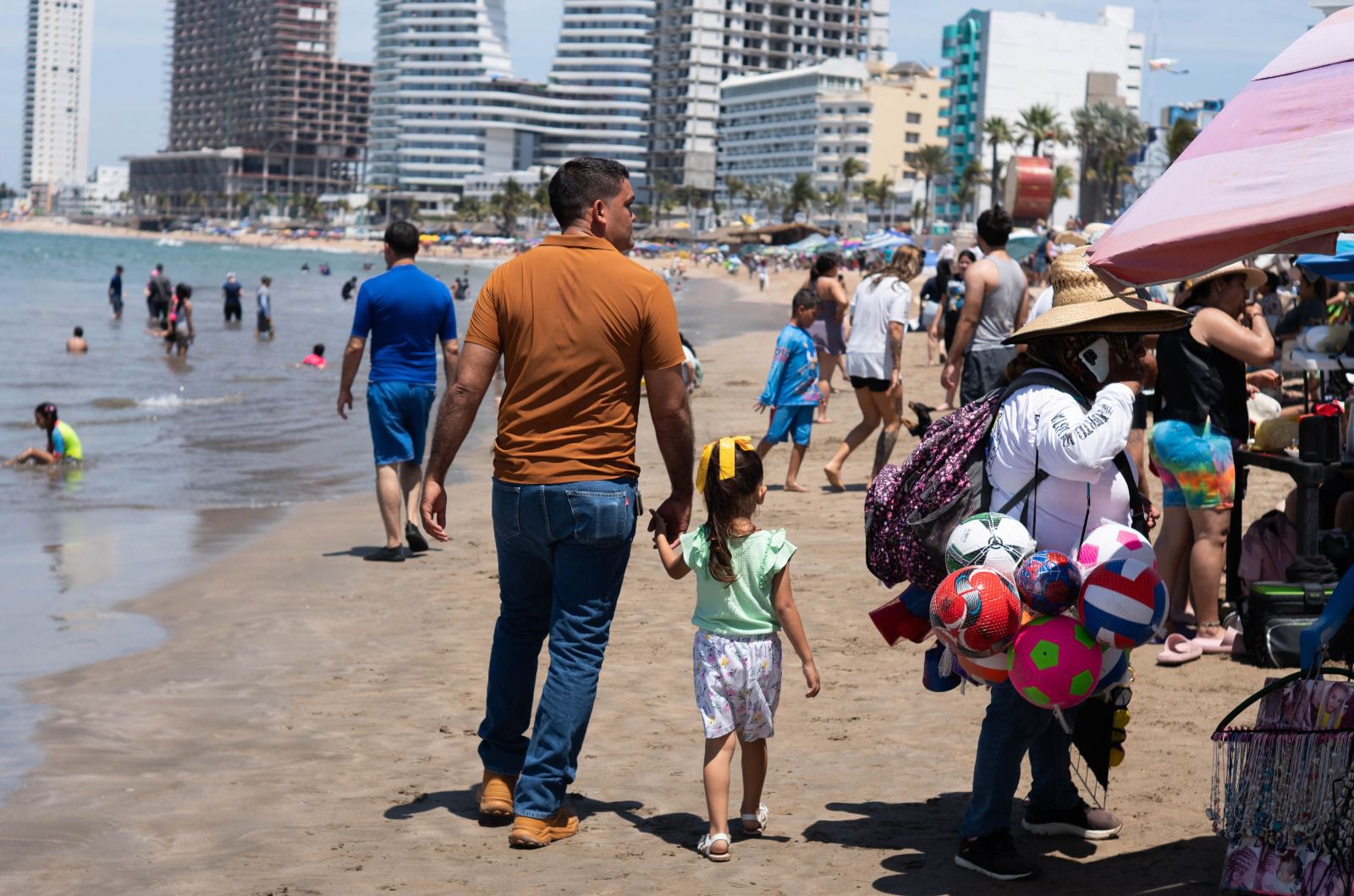 Turistas en la playa y en primer plano adulto caminando de la mano con una infante