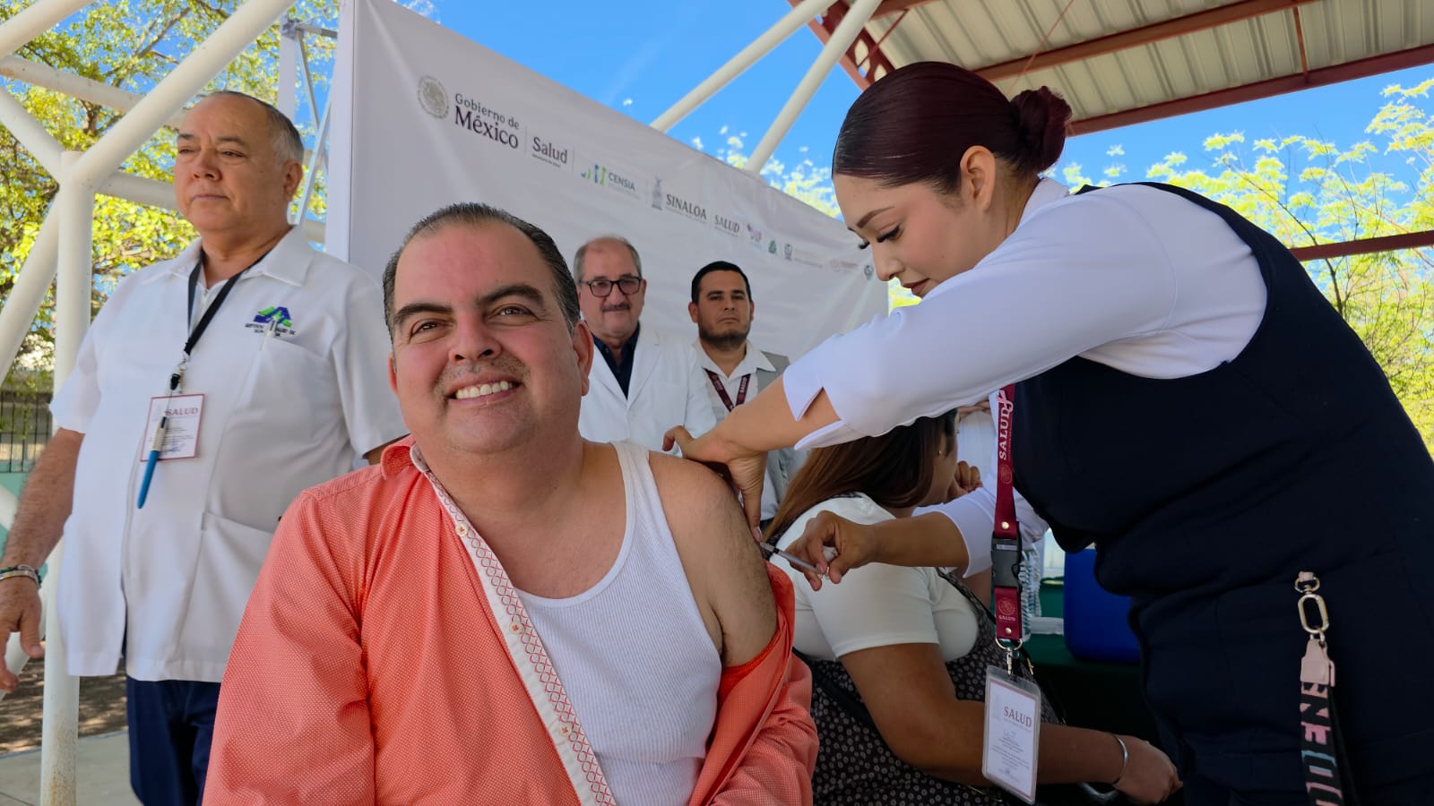 Persona con camisa naranja recibiendo una vacuna de una enfermera