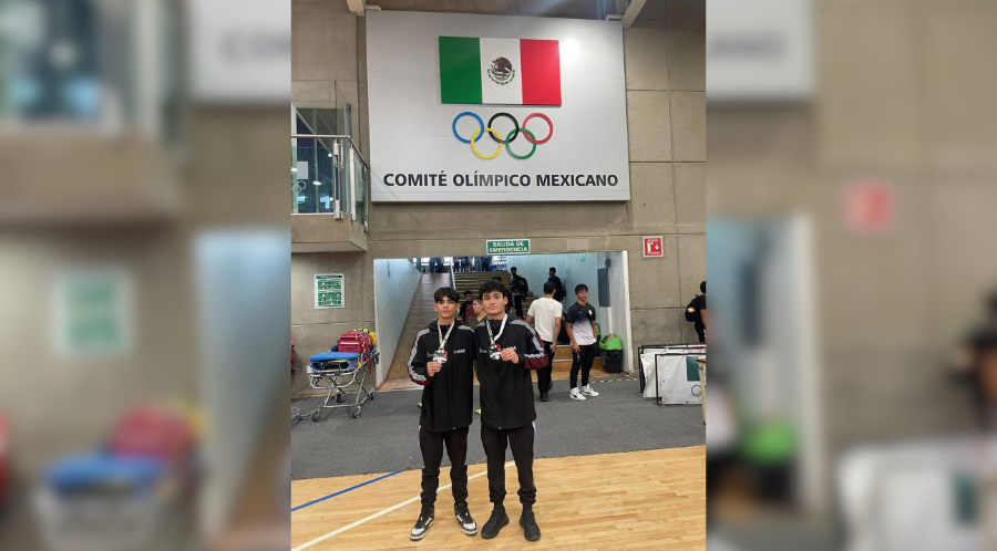 Atletas de Luchas Asociadas y al fondo una bandera de México y el logo de los Juegos Olímpicos