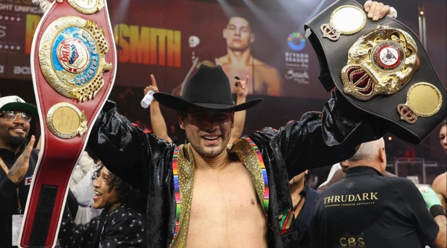 Boxeador con un sombrero vaquero negro, levantando dos títulos mundiales