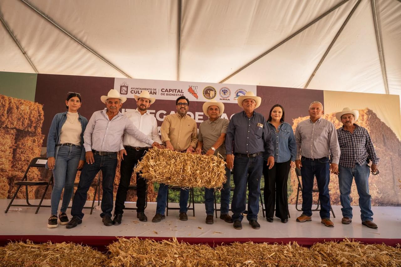 El alcalde Juan de Dios Gámez junto a otras personas en una tarima con pacas de maíz
