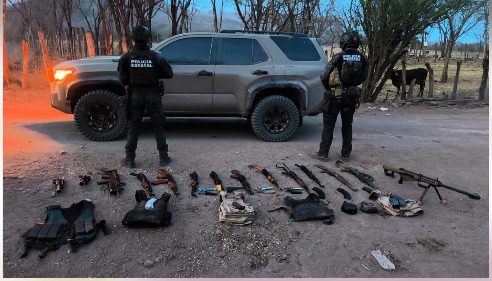 Agentes de seguridad de espaldas, en el suelo una manta y sobre ella armaas y objetos asegurados, al fondo una camioneta de color negro/gris