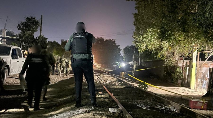 Elementos de seguridad desplegados en un camino de terracería que atraviesa una vía de trén y en una parte hay una cinta amarilla de precaución