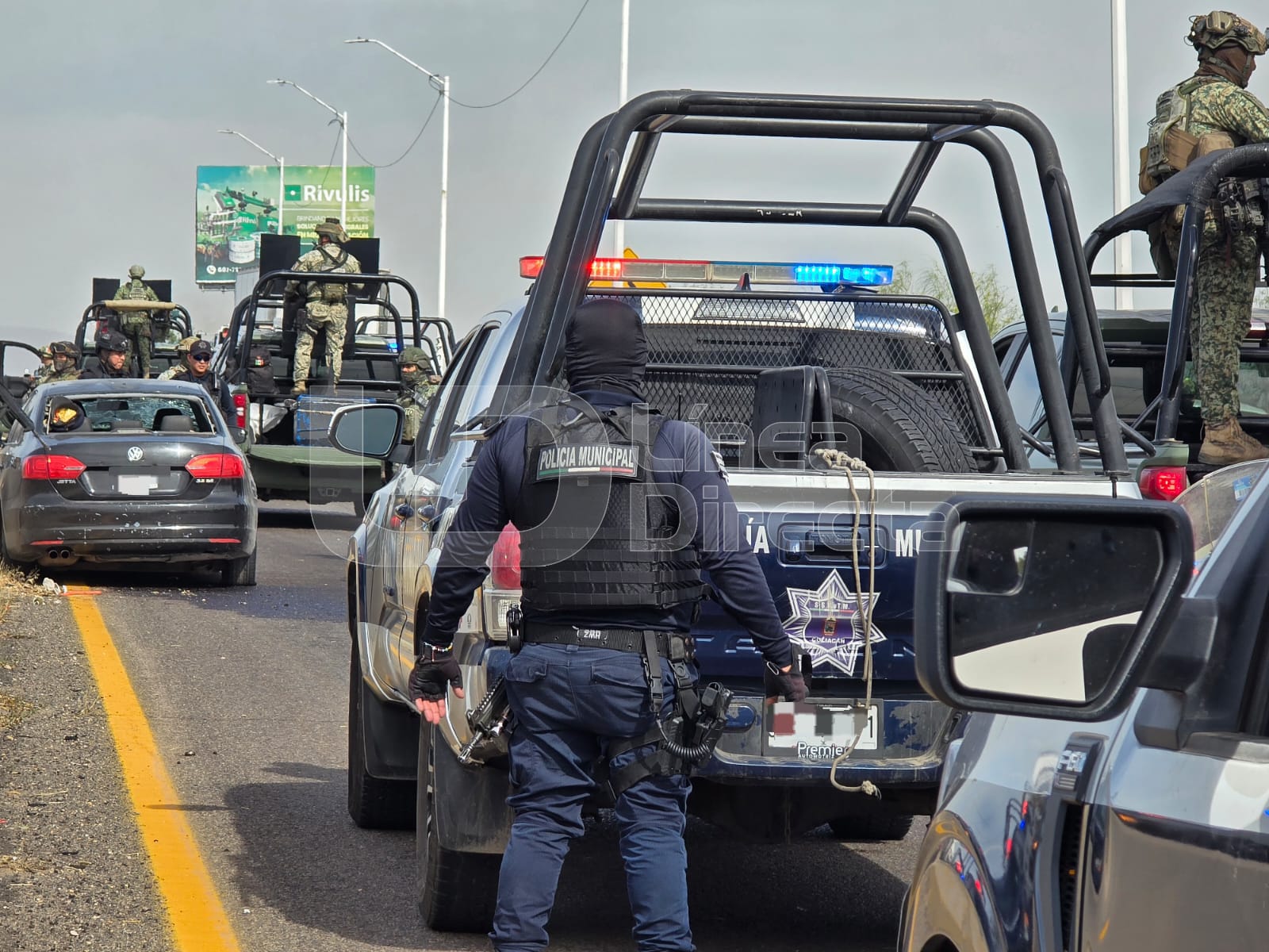 Elementos y unidades de diferentes corporaciones policiacas en una calle junto a un carro de color negro con impactos de bala