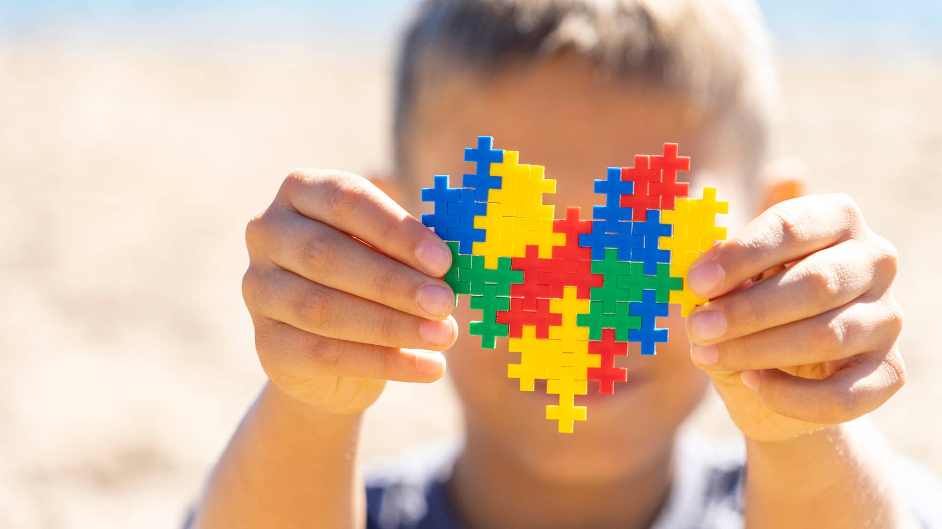 Niño sosteniendo un corazón hecho con piezas de rompecabezas de distintos colores