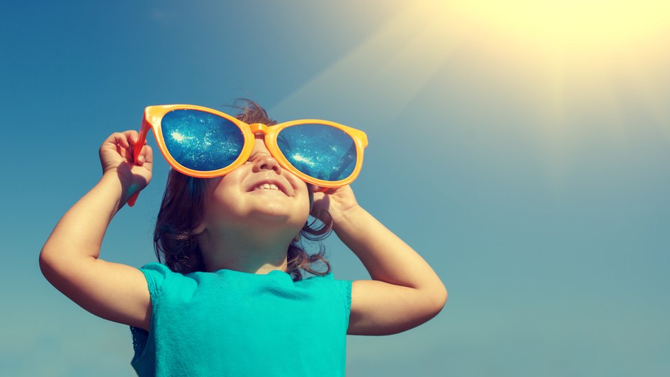 Niño con lentes de sol y al fondo un cielo azul con un sol fuerte en lo alto