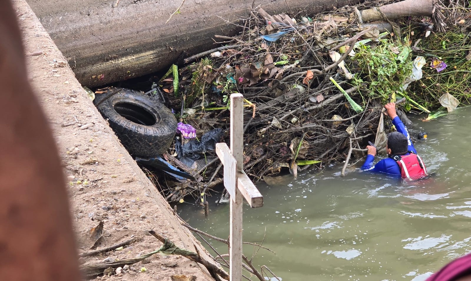 Persona en un canal junto a un bulto de ramas