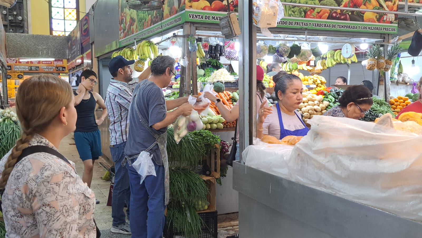 PErsonas en un mercado entre puestos de verduras