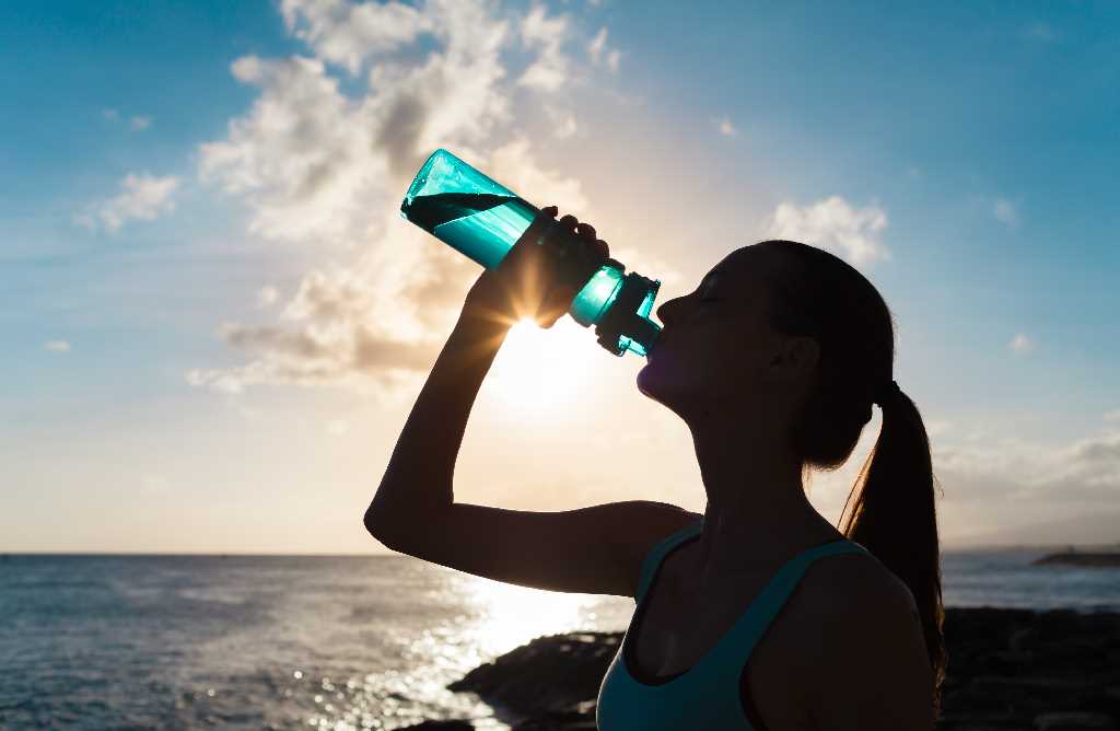 persona contra luz bebiendo agua de una botella