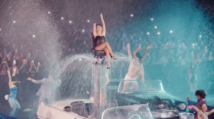 Sabrina Carpenter arriba de un auto echando agua en el escenario de Coachella junto a bailarines.