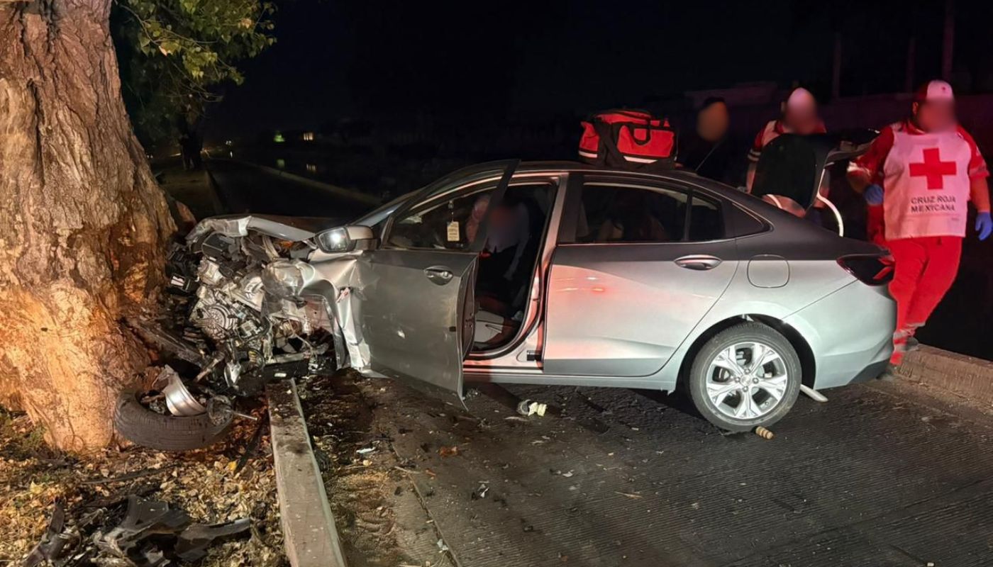 Vehículo color gris impactado contra un árbol, elementos de rescate en la zona