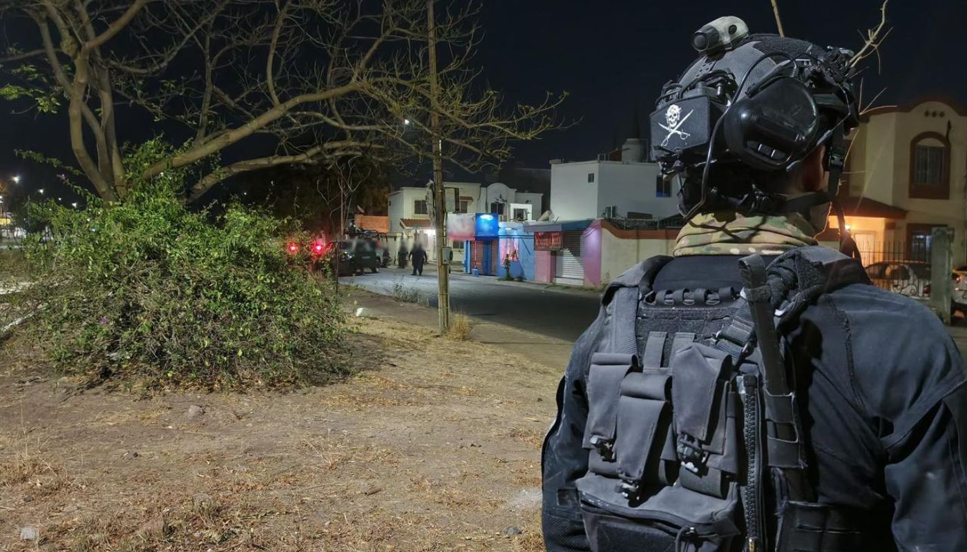 Elemento policiaco de espaldas en un camellón y al fondo más agentes y una unidad