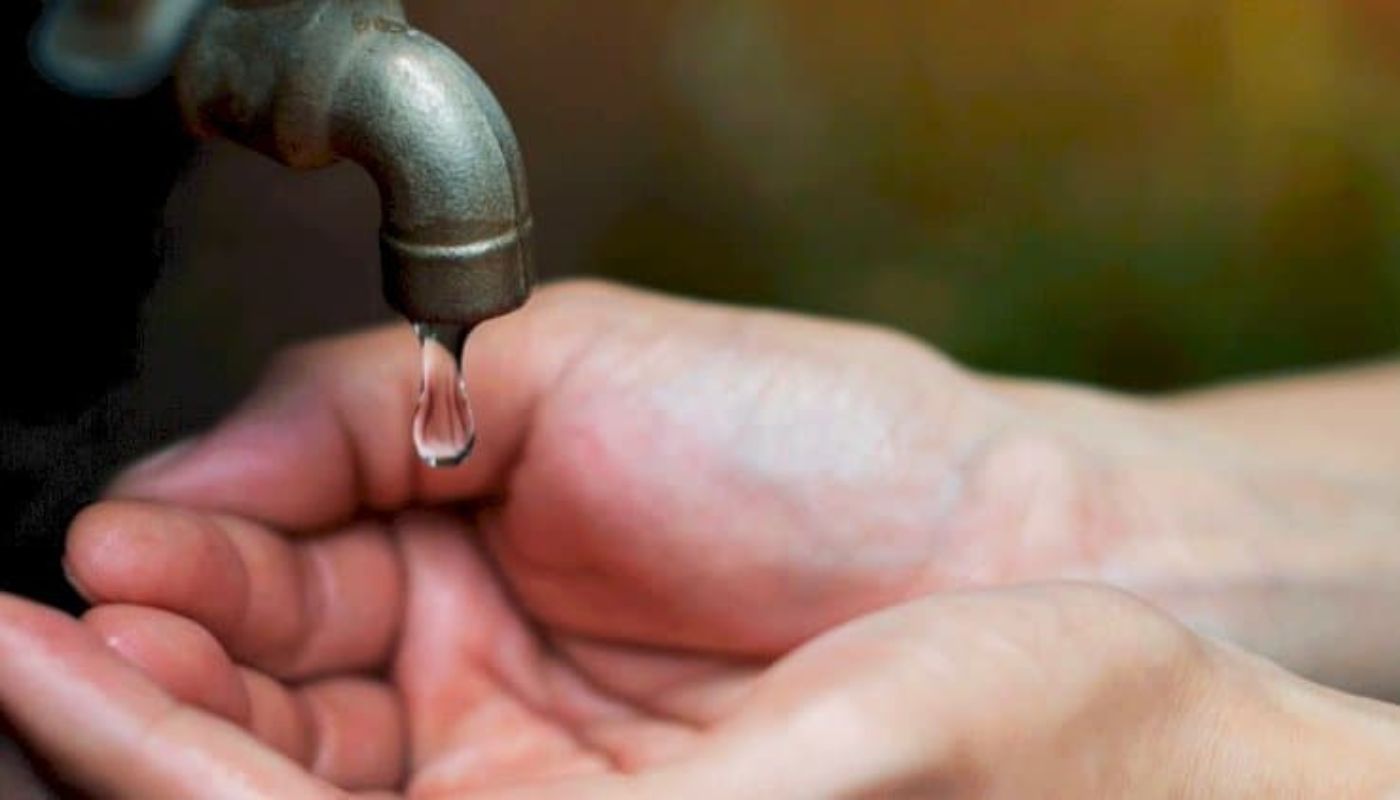 Manos de una persona debajo de un grifo del que sale una gota de agua