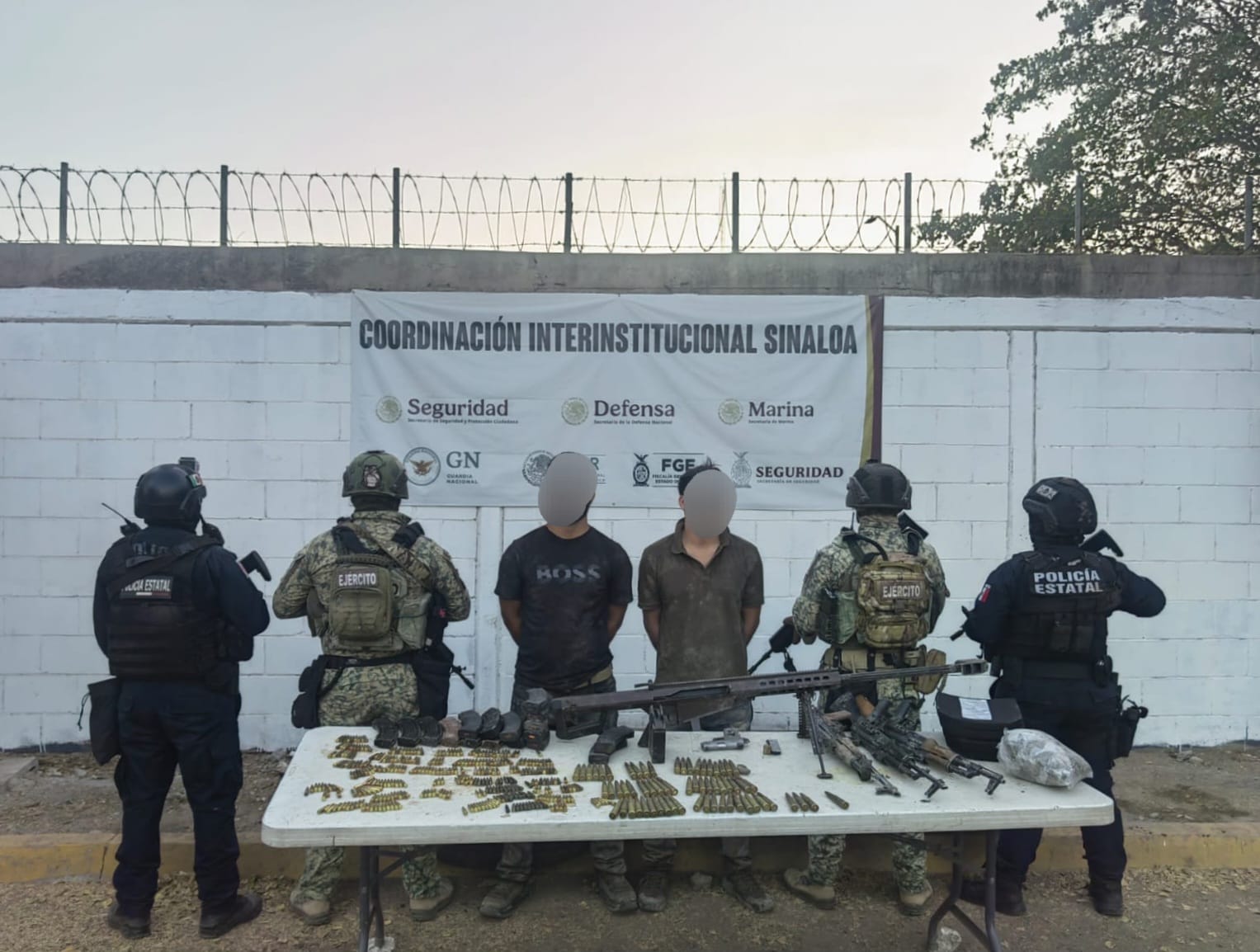 Dos personas detenidas con la cara difuminada junto a cuatro elementos de seguridad