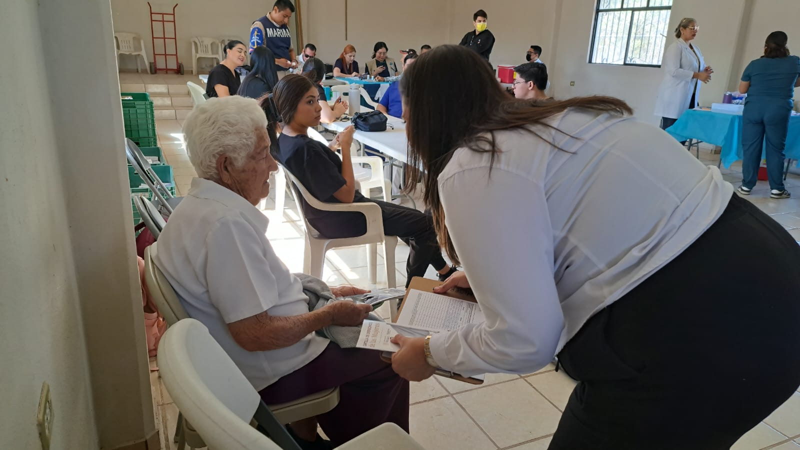 persona mayor sentada con papeles en sus manos y mujer inclinada