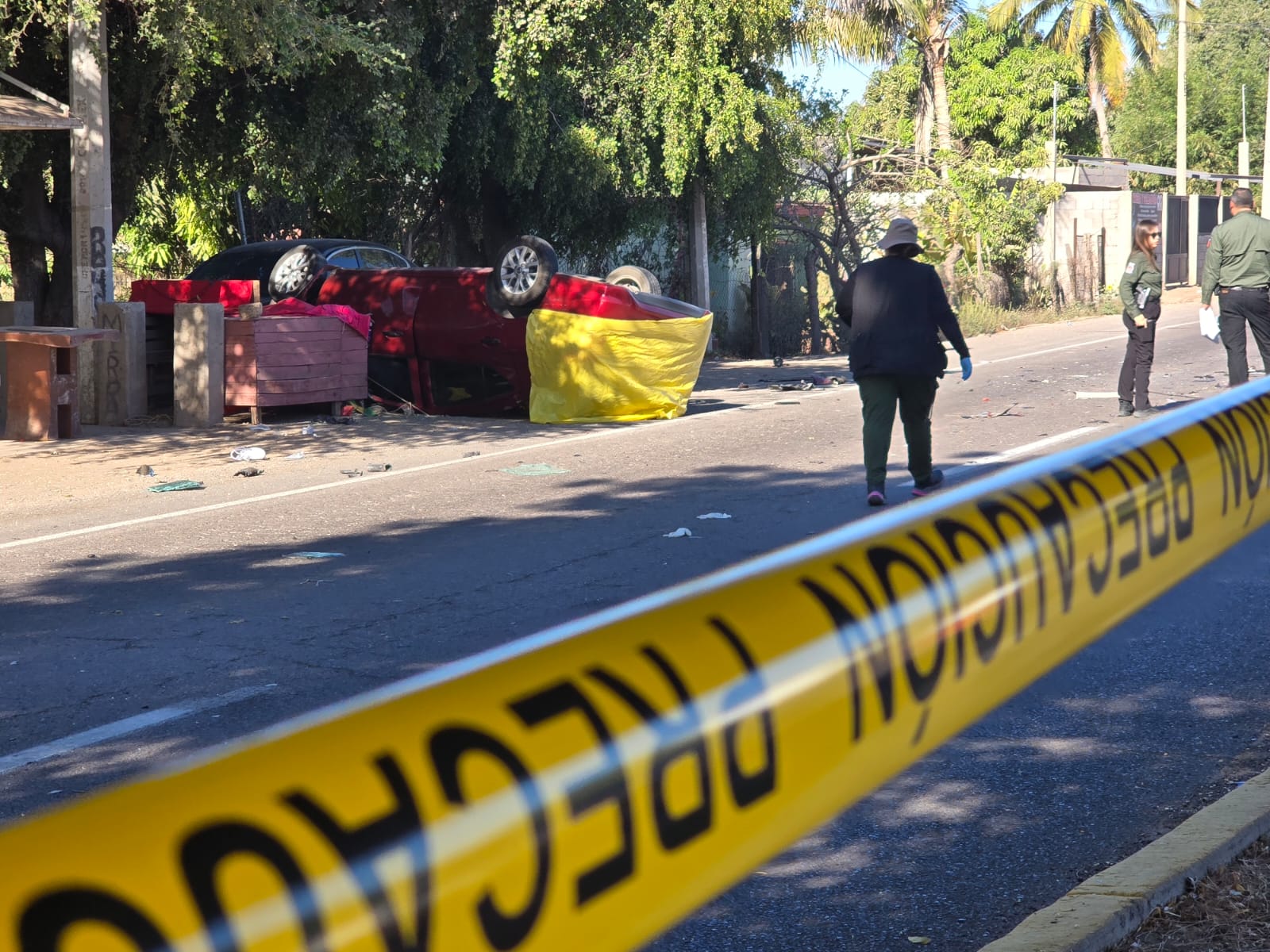 Zona asegurada con cinta amarilla y al fondo un auto volcado y autoridades custodiando la zona