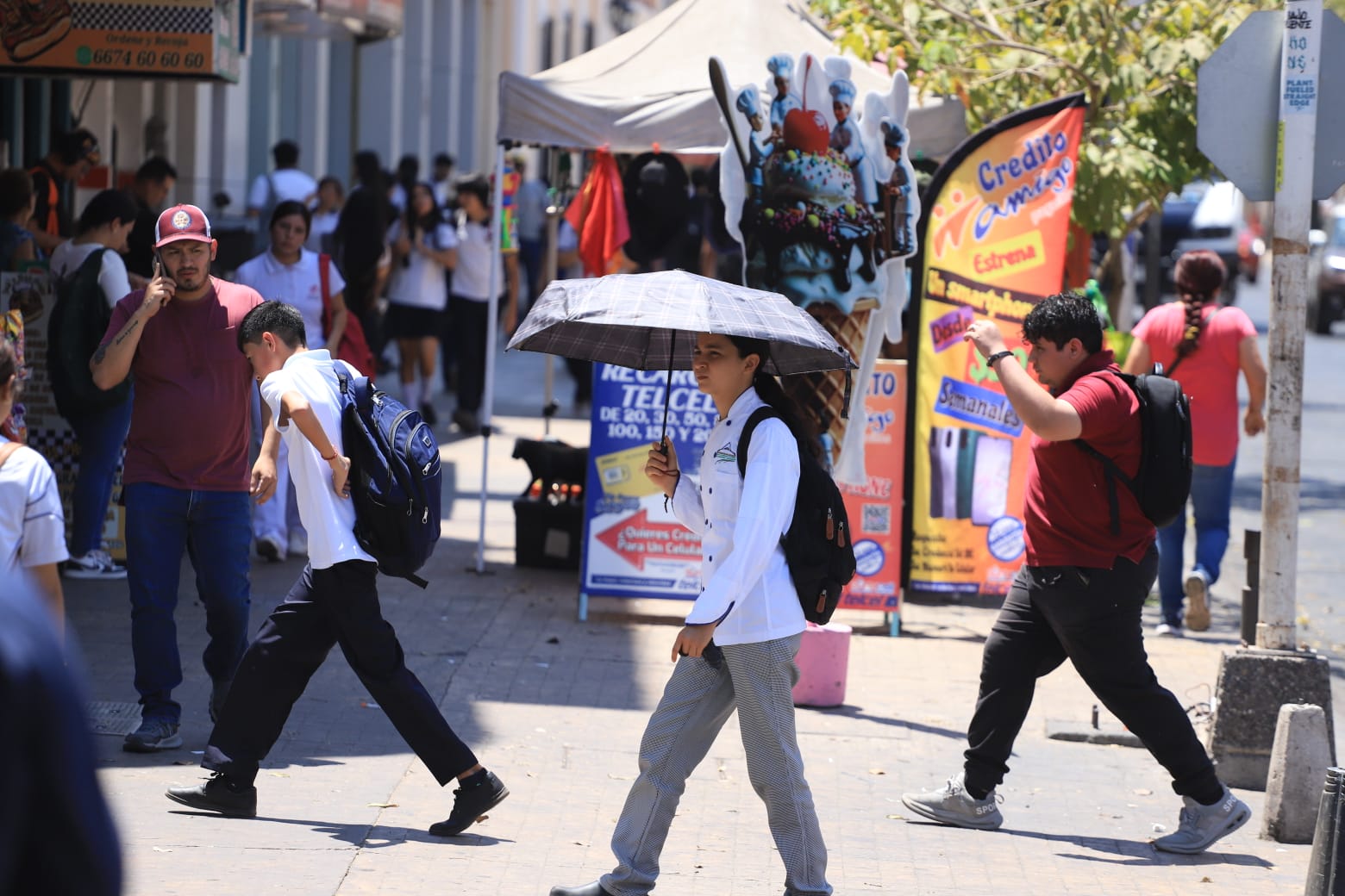 Personas caminan bajo el sol en el centro de Culiacán; una joven usa sombrilla para protegerse de las altas temperaturas y sensación térmica extrema.