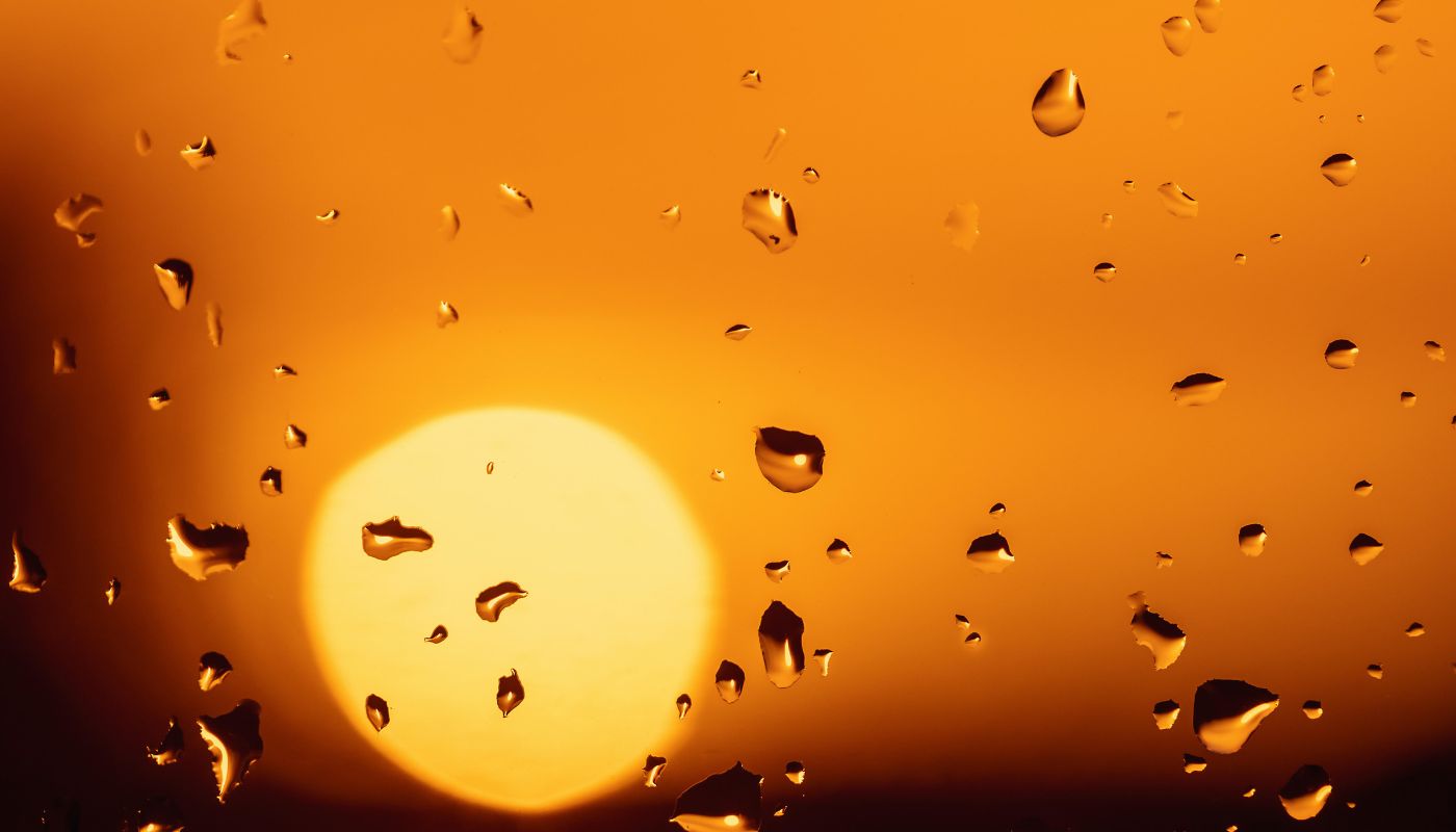 vidrio de una ventana con gotas de agua por la lluvia y al fondo el sol fuerte