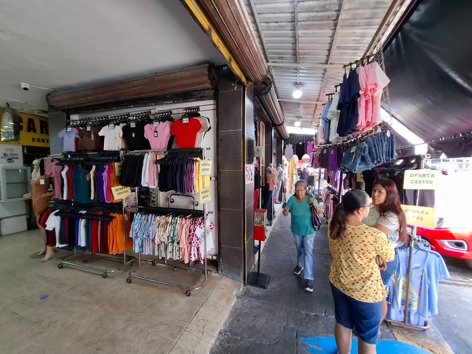Local con ropa colgada en la pared para exhibición y personas paradas en la banqueta