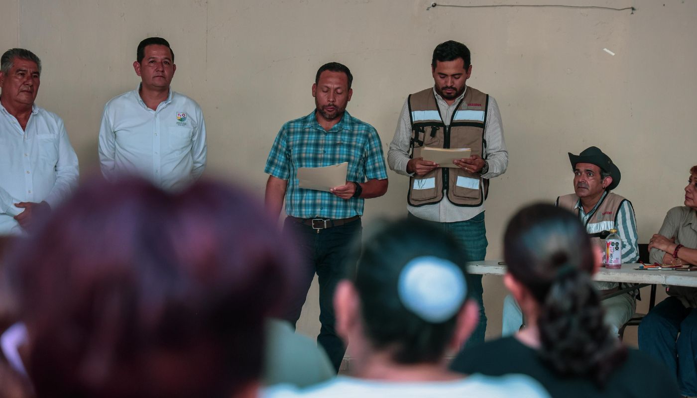 Personas de pie con documentos en las manos frente a un grupo de personas