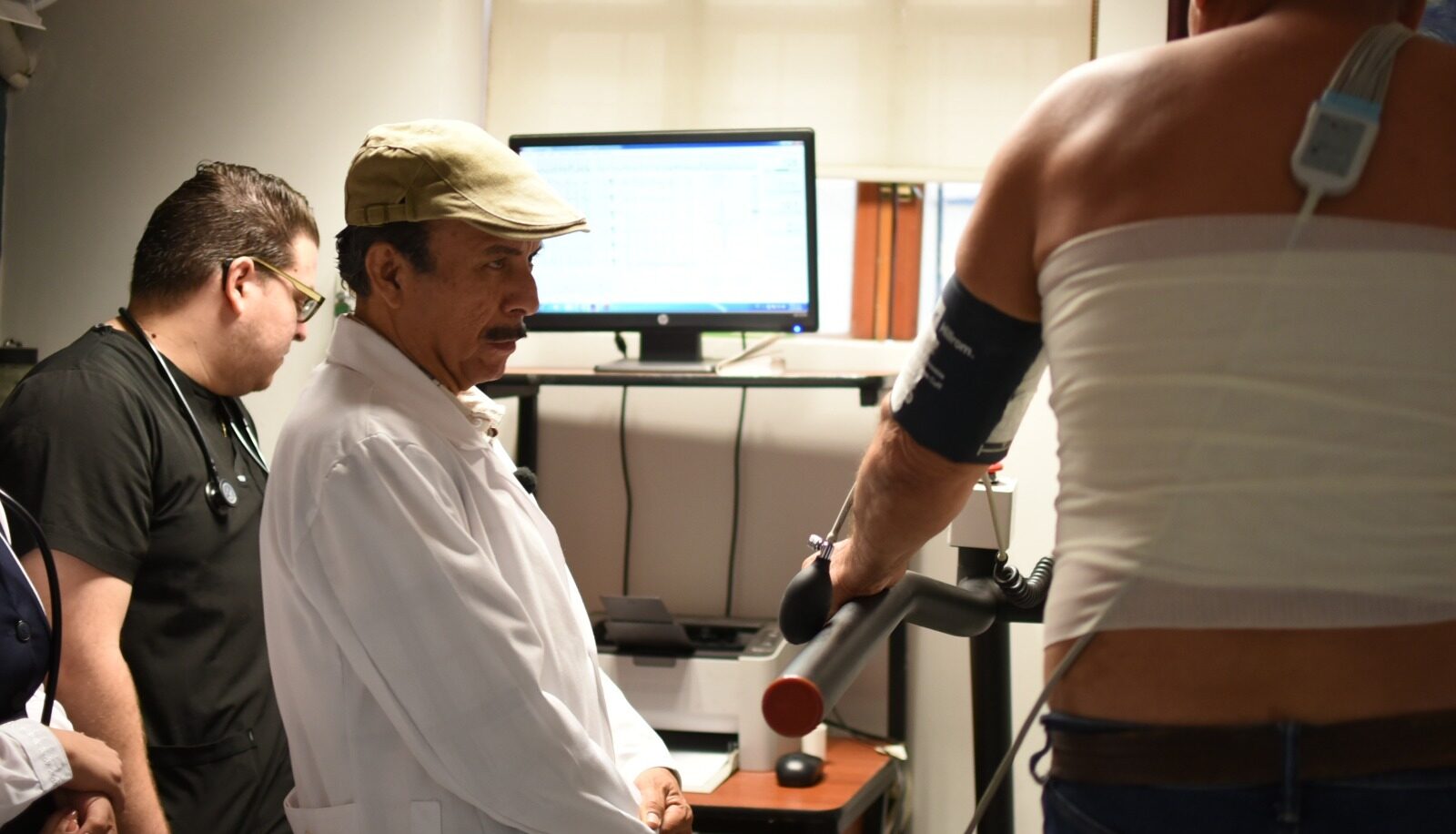 Doctor en consulta de cardiología junto a una persona con un medidor de presión en el brazo izquierdo