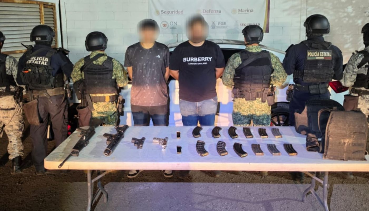 Civiles detenidos en el medio y a las orillas elementos de seguridad de espaldas, en una mesa al medio armas y artefactos confiscados