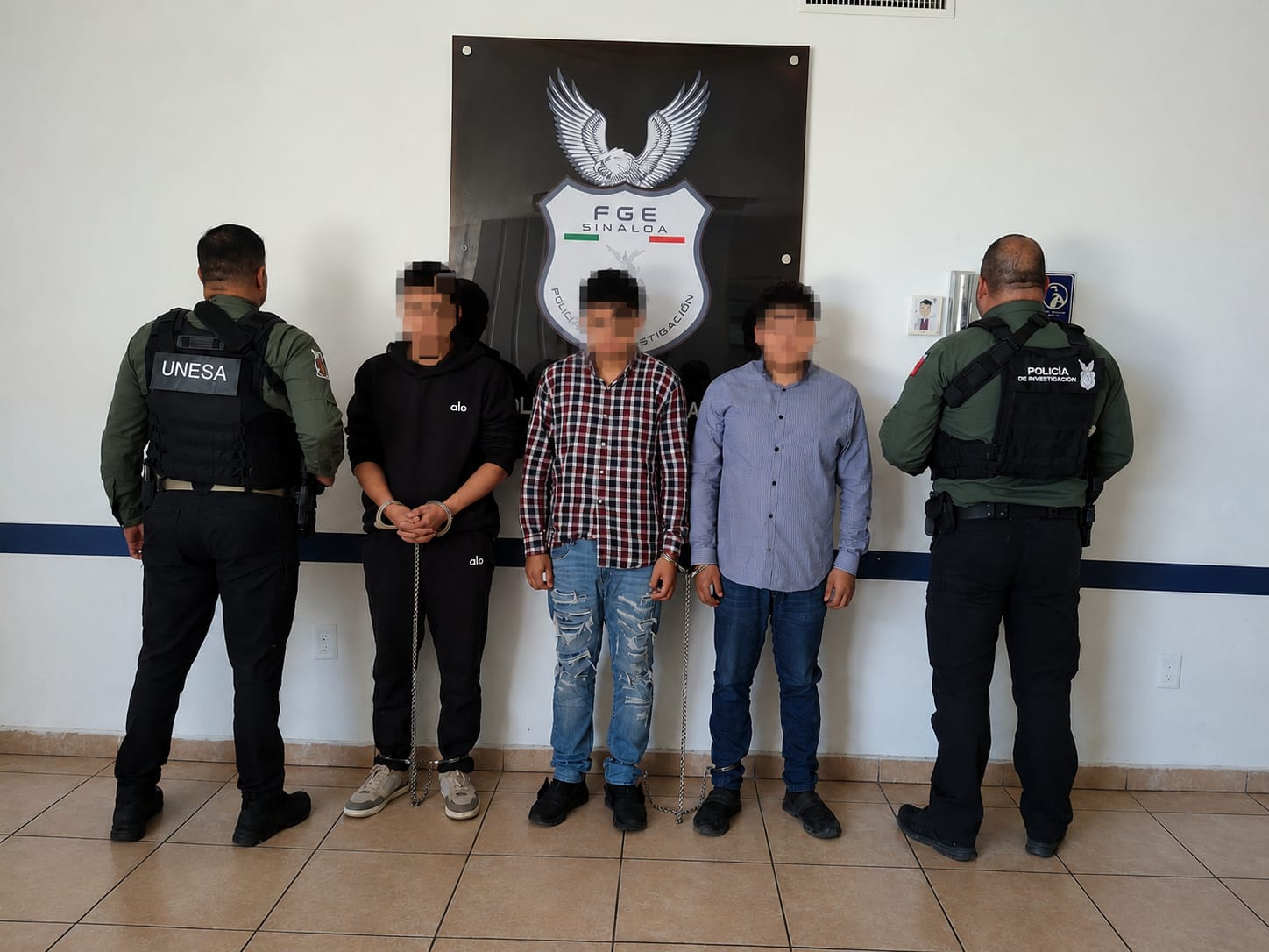 Tres personas detenidas con la cara difuminada junto a dos personas de seguridad