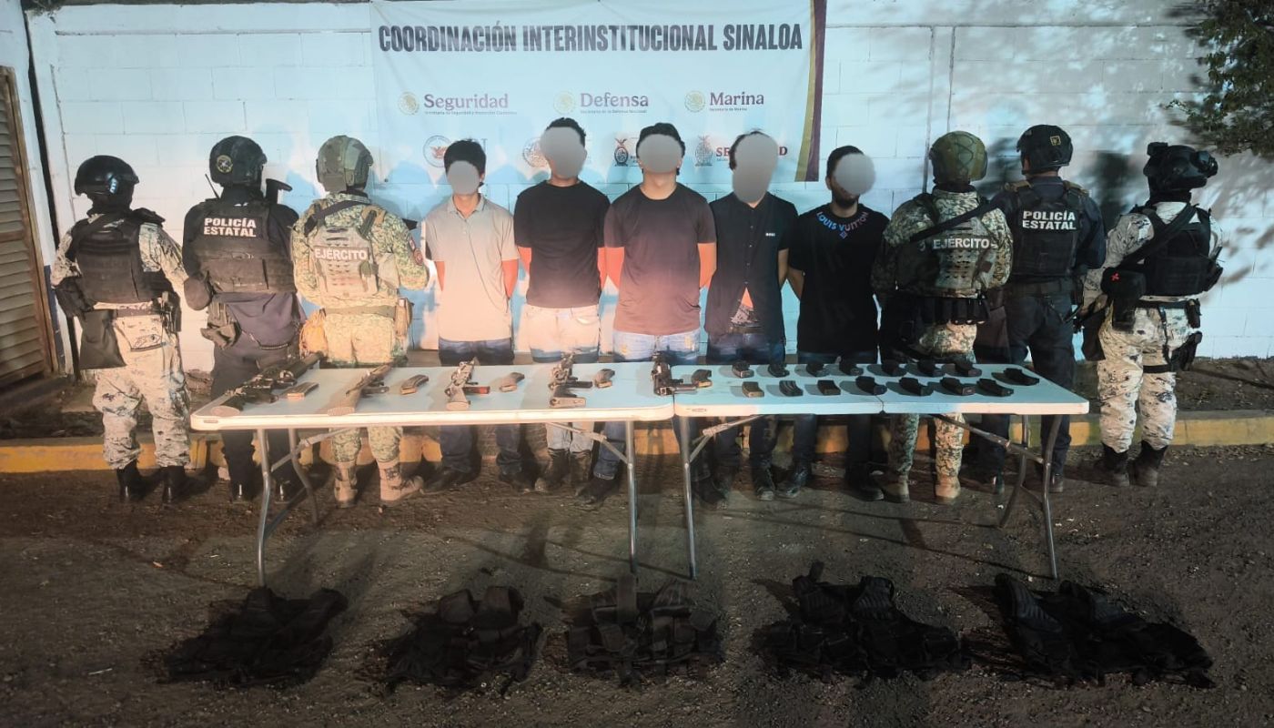 Personas con el rostro cubierto y las manos esposadas y a los costados agentes policiacos y en una mesa objetos asegurados