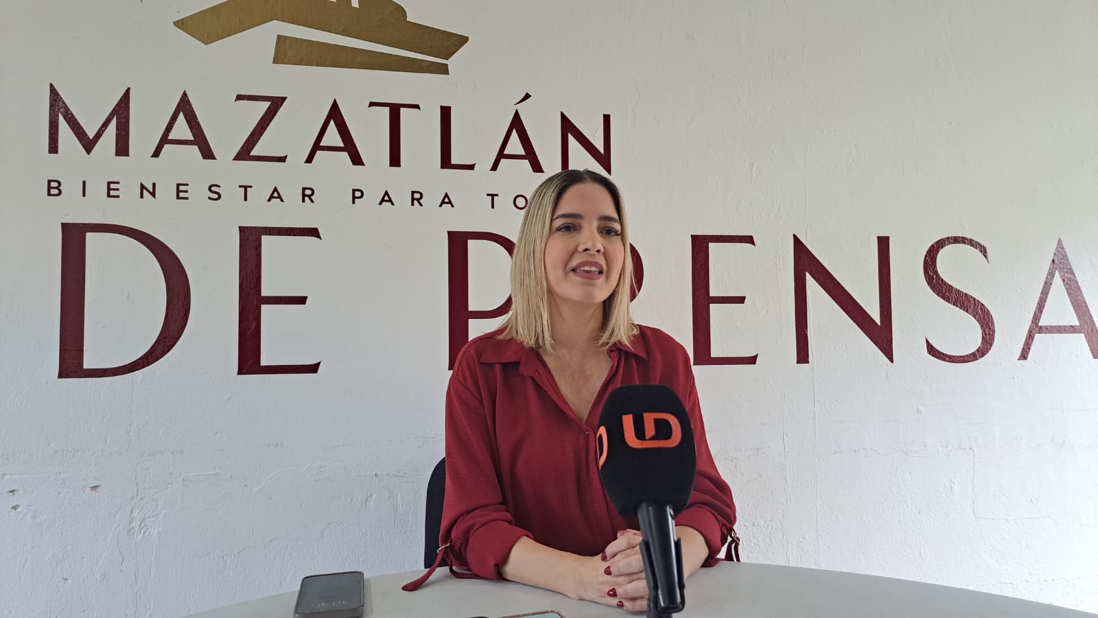Alcaldesa de Mazatlán junto a un micrófono de Línea Directa y detrás el logo del Ayuntamiento de Mazatlán
