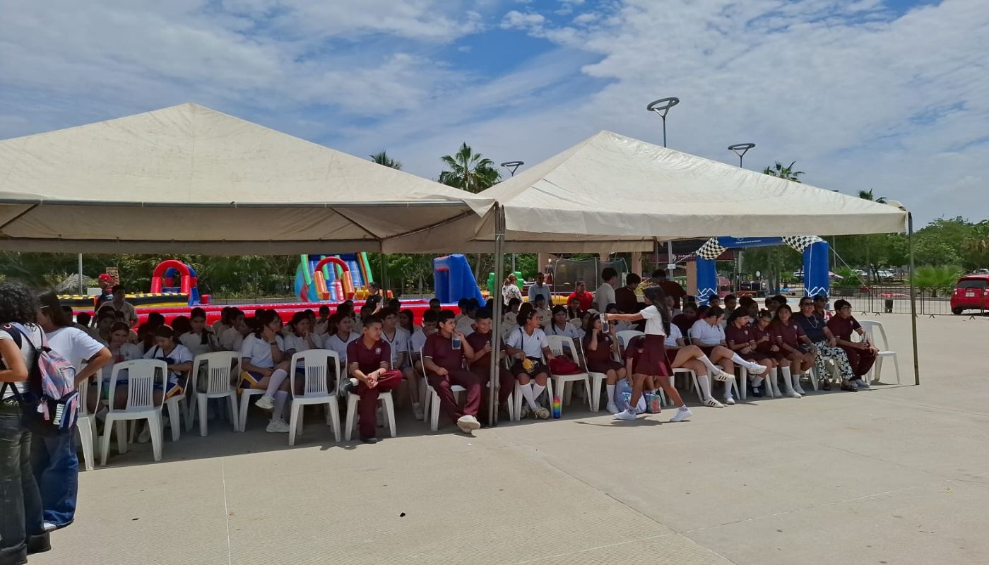 Estudiantes sentados bajo una carpa, en una explanada