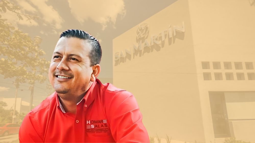 Al frente Homar Salas sonriendo y detrás de el una casa funeraria
