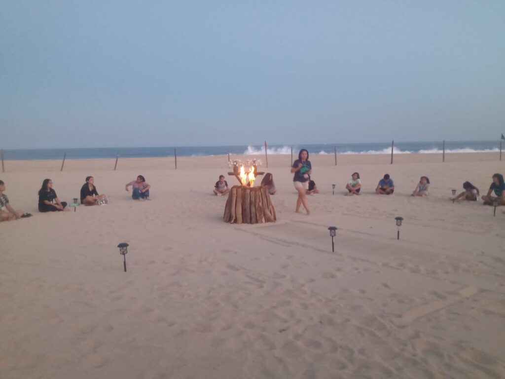 Arena en la playa junto a un circulo de personas y en el centro una fogata