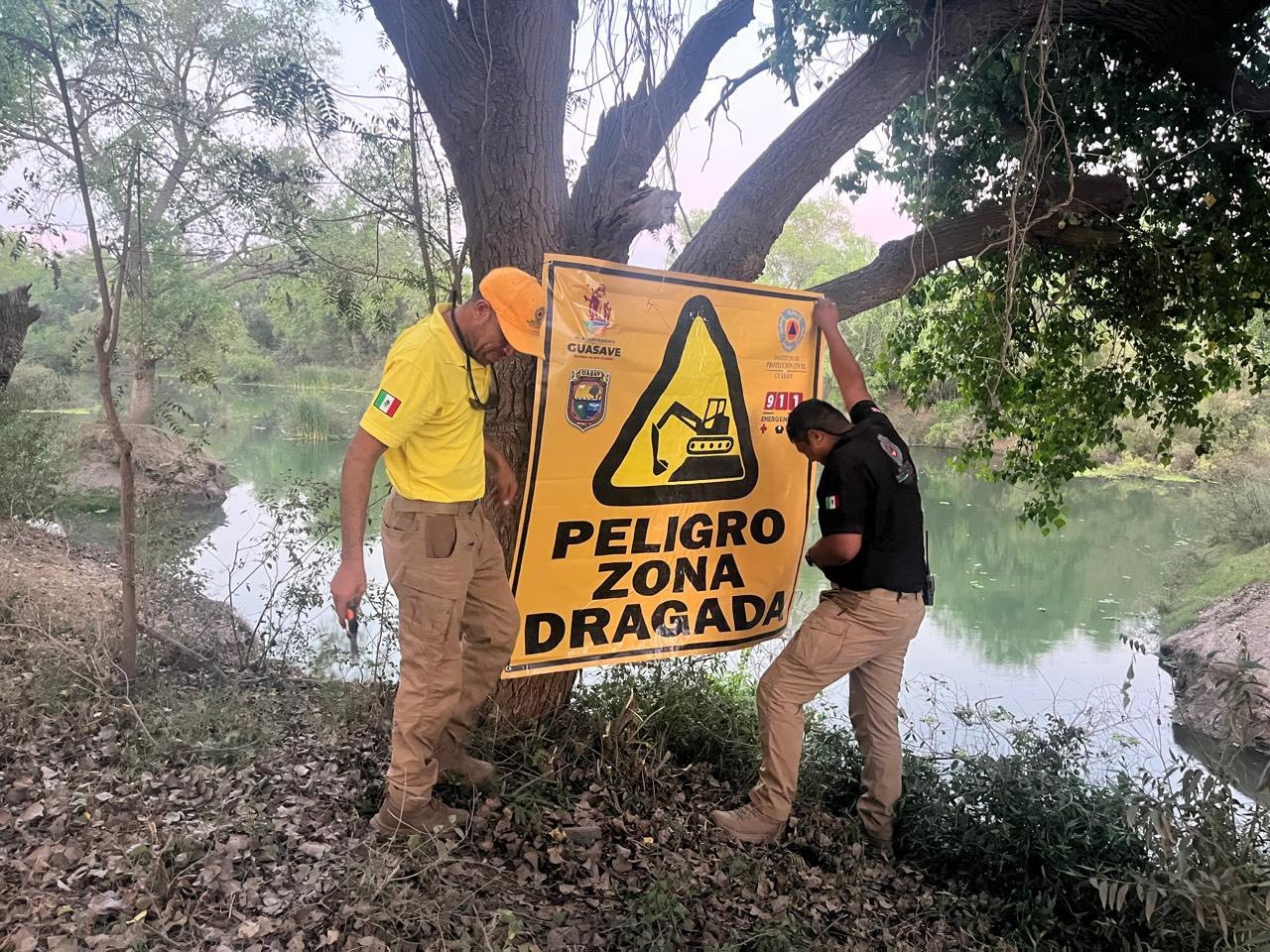 Dos personas con una lona con Peligro color amarillo