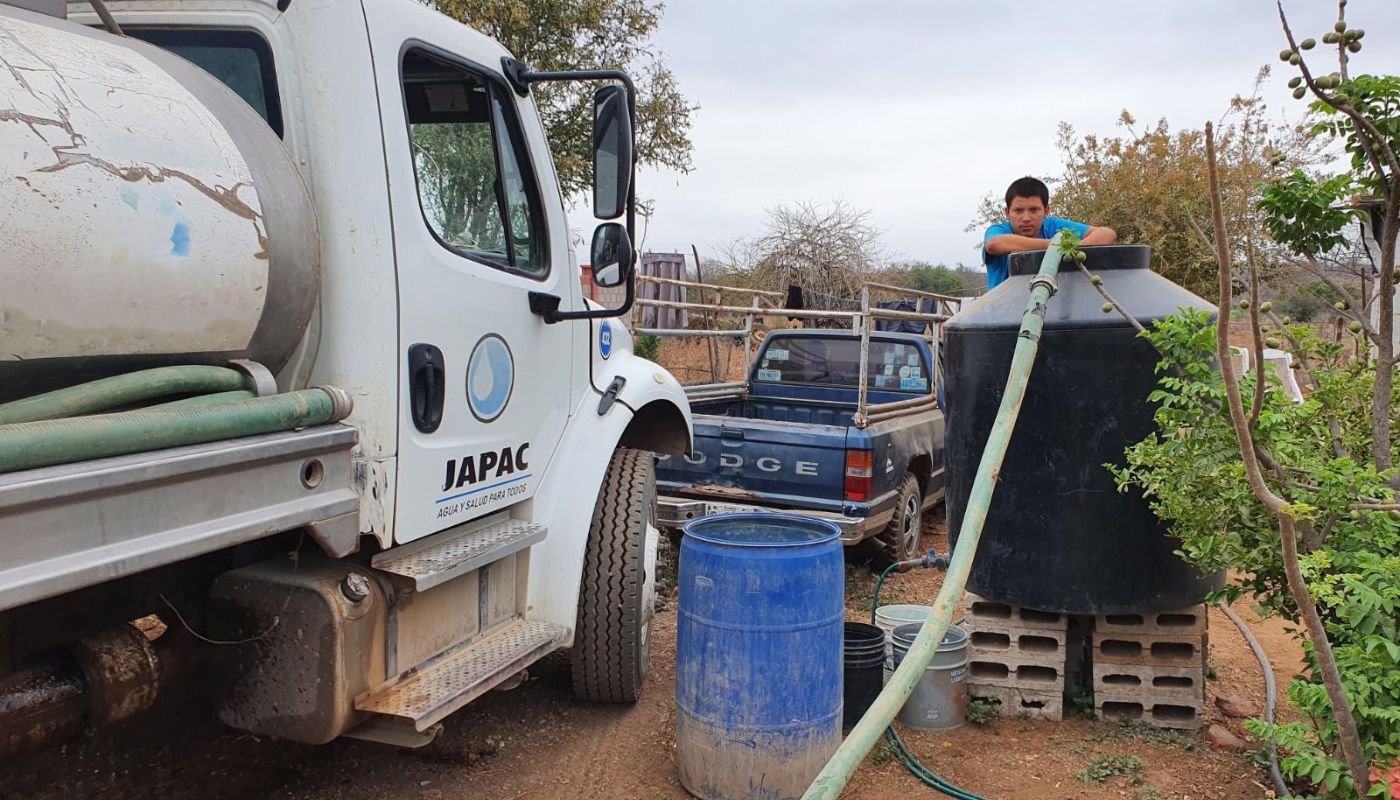 Persona vertiendo agua en un contenedor y una unidad pipa de agua