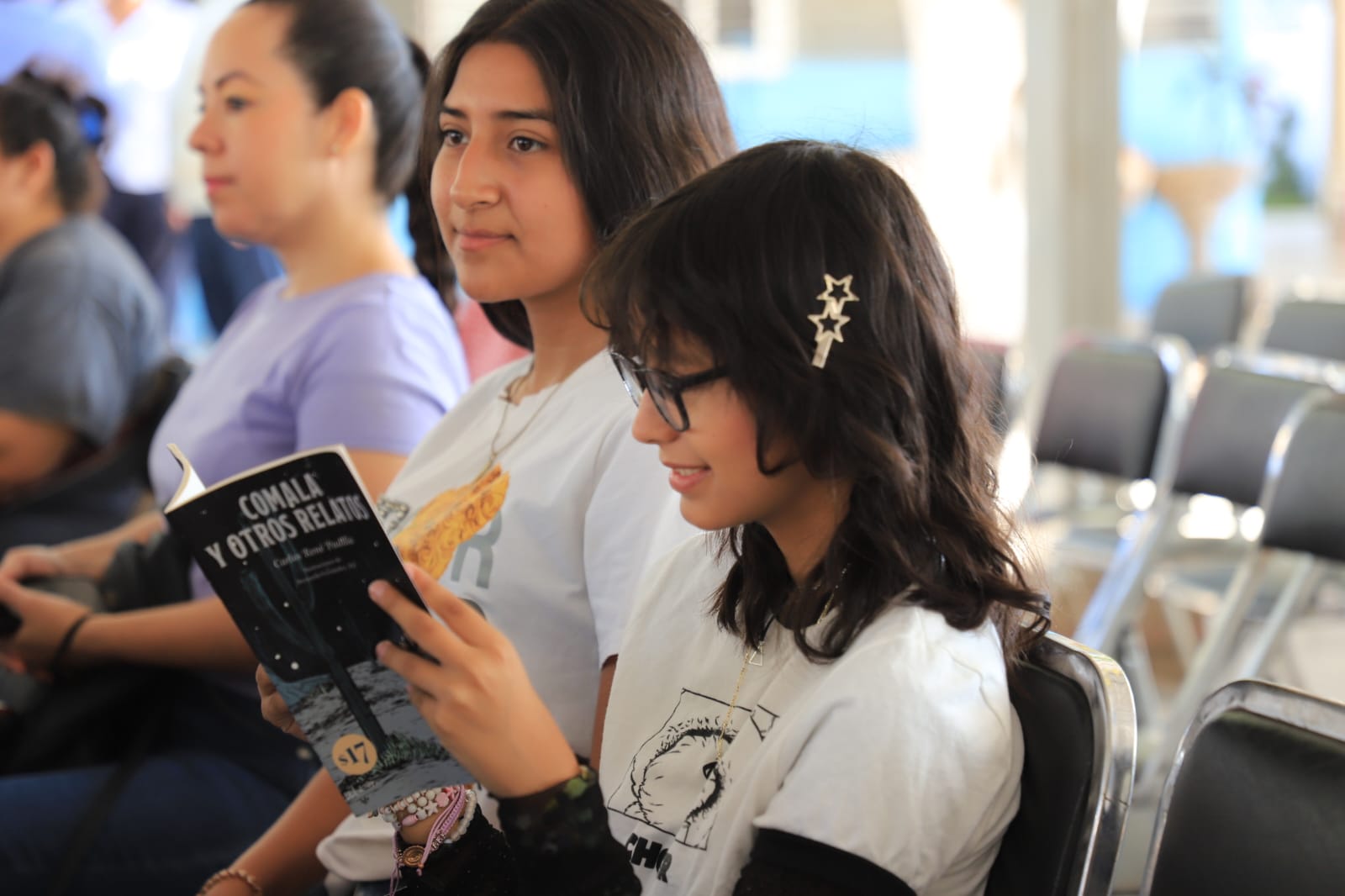 Niñas sentadas en un lugar y una de ellas leyendo un libro