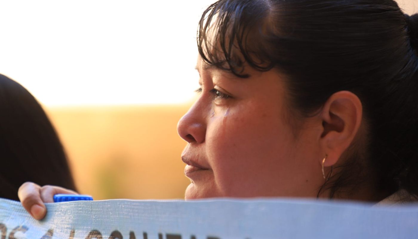 Mujer sosteniendo una pancarta con la mirada hacia el frente y una lagrima brotando de su ojo