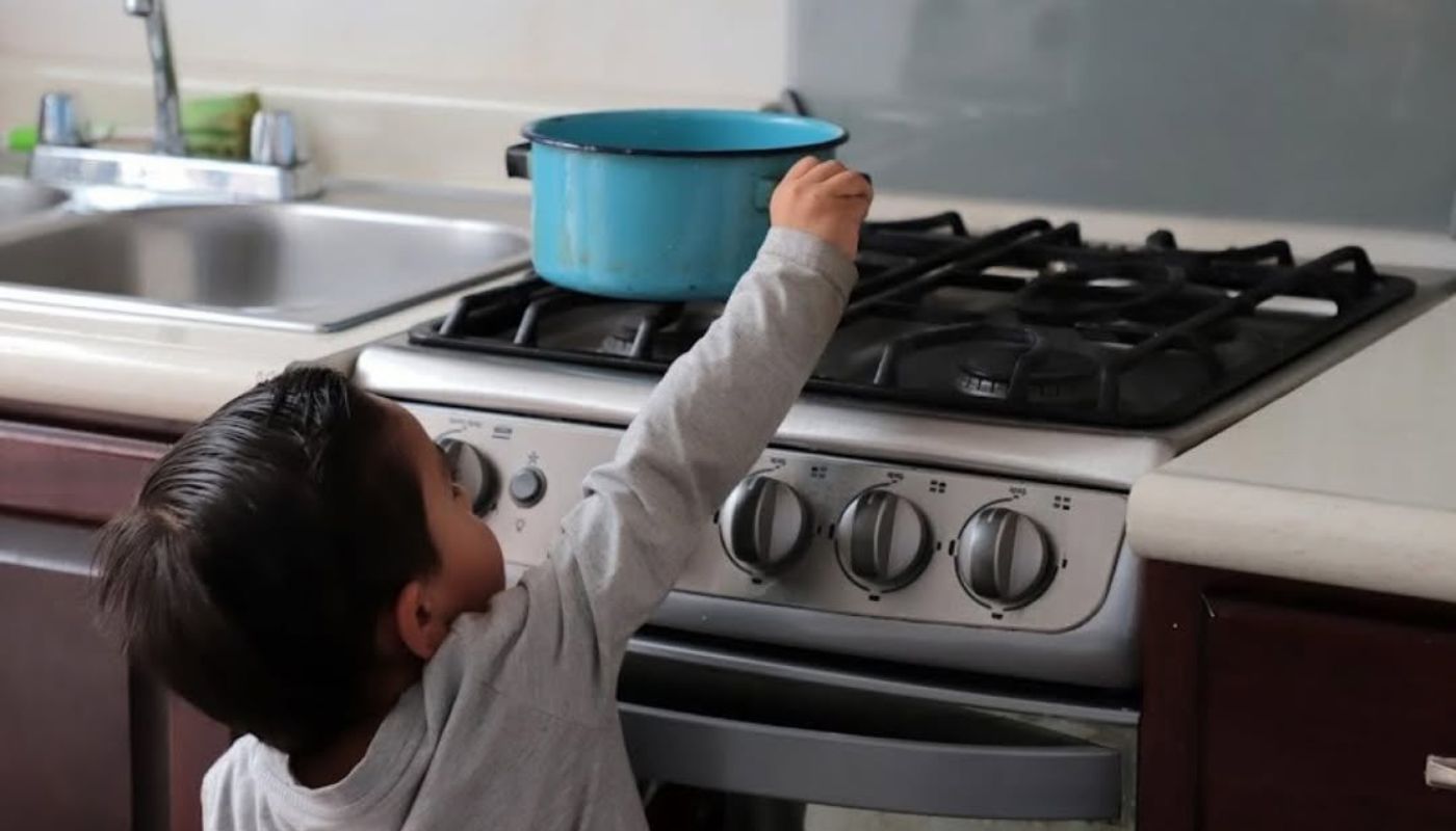 Niño en una estufa agarrando una olla de color azul