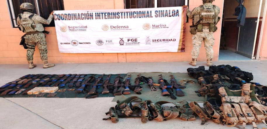 Agentes militares sosteniendo una lona y en el suelo otra lona con objetos y armas